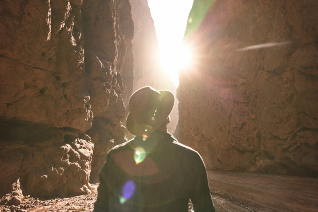 a man standing in a canyon with the sun shining through the rocks